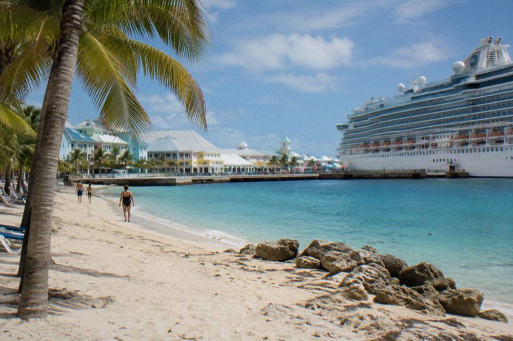 Sandy public beach along the Nassau waterfront with calm shallow water and scattered palm trees